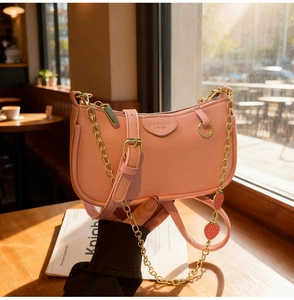 Détail du sac bandoulière rose avec chaîne fraise dorée sur une table en bois