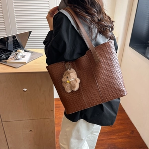 Brown woven leather tote bag with a cute plush bear pendant for autumn commute style
