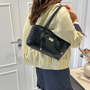 Minimalist black crocodile embossed underarm bag with gold plaque on a model's shoulder