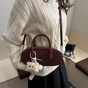 Minimalist burgundy pillow bag with plush charm shown in a cozy lifestyle setting