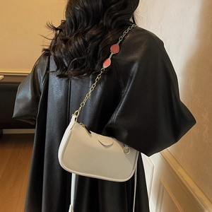 Sac hobo blanc avec chaîne dorée et breloques fraise sur un modèle en veste en cuir