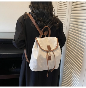 Detailed back view of a minimalist canvas backpack with brown leather flap and straps