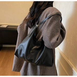 Detail of minimalist black leather hobo bag with adjustable strap worn on an overcoat