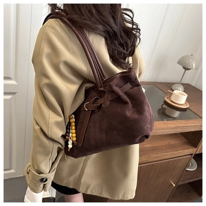 Detail of dark brown suede tote bag featuring a leather strap and wooden bead charm accent