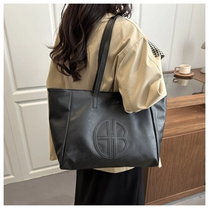 Detail view of a large black tote bag with embossed logo on a model in a cafe setting