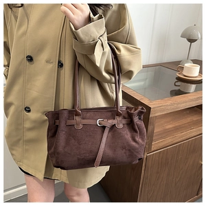 Detail of vintage brown suede tote bag with metal buckle on a model in a cozy room