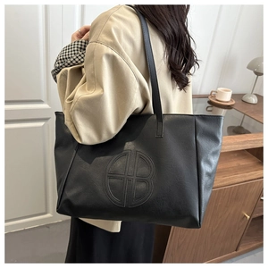 Detail of a large black tote bag featuring a circular B logo embossing on pebbled leather