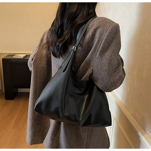 Minimalist black oversized tote bag worn over the shoulder with a textured suit