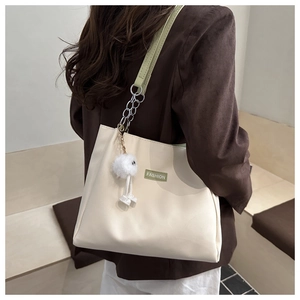 Detail of beige tote bag with green strap, fashion patch and white pompom pendant