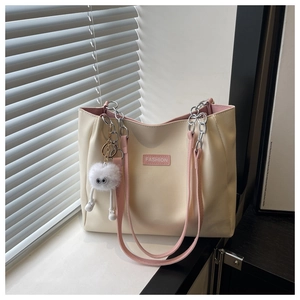 Detail of a beige tote bag with pink straps, fashion tag, and fluffy charm on a windowsill