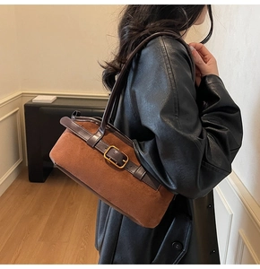 Close-up of a brown suede rectangular shoulder bag with leather buckle on a black coat