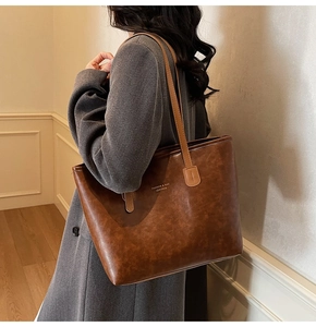 Close-up of a large vintage brown leather tote bag worn by a model in a grey wool coat