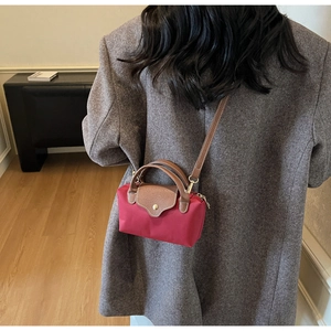 Detail of red nylon crossbody bag with brown leather handles worn by a model