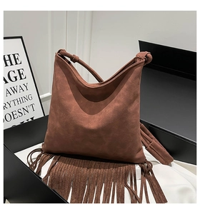 Détail d'un sac à bandoulière en daim marron à franges sur soie blanche et boîte noire chic