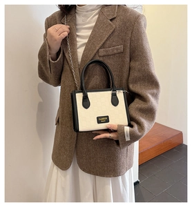 Détail de la texture damier sur un sac crème avec poignée noire et bandoulière chaîne