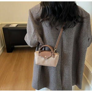 Model wearing a mini beige nylon crossbody bag with brown leather flap and top handle