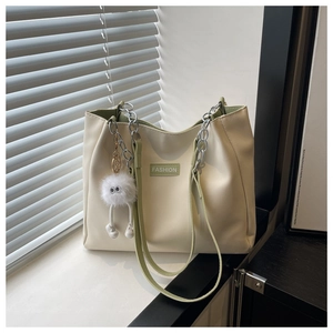 Detail of off-white tote bag with green accents, chain strap and plush monster charm
