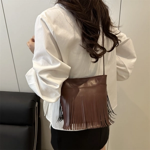 Sac seau vintage marron foncé à franges porté par un mannequin au style épuré