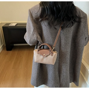 Mini beige nylon crossbody bag with brown leather flap worn by a model in a cozy room