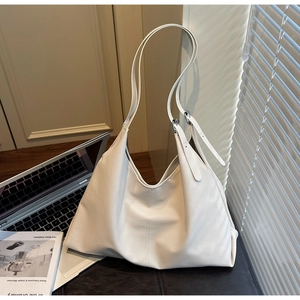 Close-up of a white minimalist hobo shoulder bag with silver buckle on a workspace desk