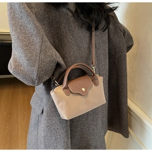 Side view of beige nylon mini crossbody bag with brown leather handles on wool coat