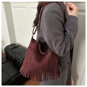 Detail of burgundy tassel crossbody bag with suede texture on grey tweed blazer