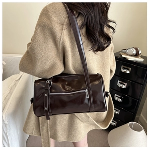 Détail d'un sac cylindrique marron foncé brillant avec boucles argentées porté par un mannequin