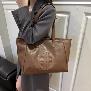 Minimalist large capacity brown tote bag with embossed logo worn on shoulder