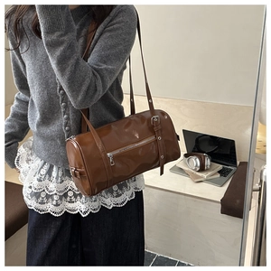 Gros plan d'un sac cylindrique marron en cuir brillant porté par un mannequin