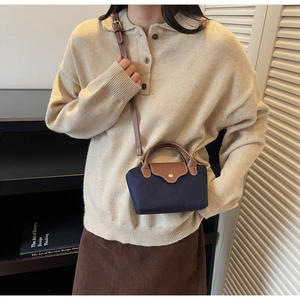 Fashionable mini navy nylon crossbody bag with brown leather accents on beige sweater