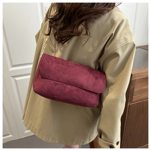 Dettaglio borsa a tracolla bordeaux in camoscio con catena oro su un cappotto kaki casual