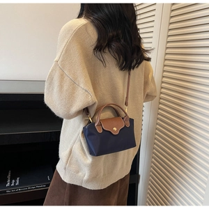 Detail of navy nylon crossbody bag with brown leather handles and adjustable strap