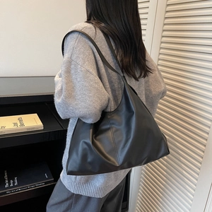Minimalist black large capacity tote bag in soft leather shown on a model's shoulder