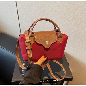 Detailed close-up of burgundy nylon bag with brown leather flap and gold snap button