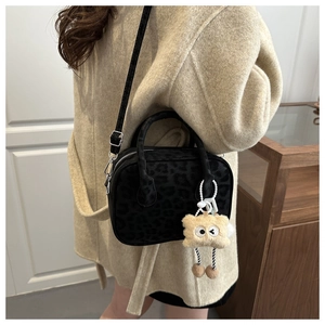 Detail of black leopard print crossbody bag with cute plush charm on a beige coat