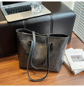Detail of a charcoal gray matte leather tote bag with fine stitching and gold lettering