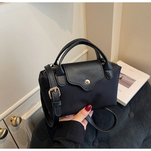 Detail of a black nylon mini bag with leather trim and gold buckle being held by hand