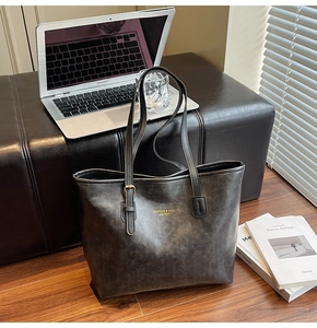 Detail of large dark grey vintage leather tote bag on a bench with lifestyle items