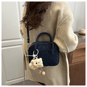 Detail of dark blue leopard print crossbody bag with cute plush pendant on a beige coat