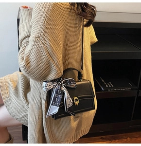 Dettaglio borsa quadrata in pelle nera con fibbia ad anello oro e foulard di seta sul manico
