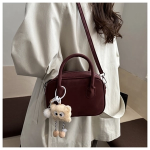 Close-up of a burgundy matte shoulder bag with a cute plush bear charm on a model