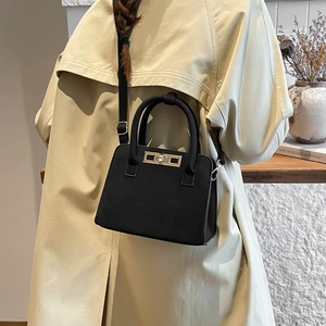 Elegant black suede tote bag with gold hardware worn by a model in a beige trench coat