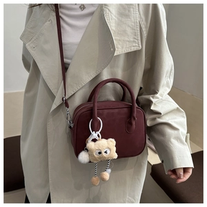 Close-up of a dark red square bag with round handles and a cute bear charm detail