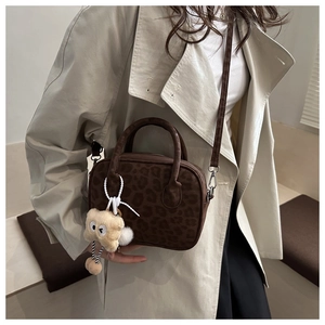 Detail of leopard print handbag with plush charm on a model's beige winter coat