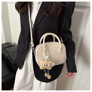 Model wearing a minimalist cream leather crossbody bag with a cute brown plush charm