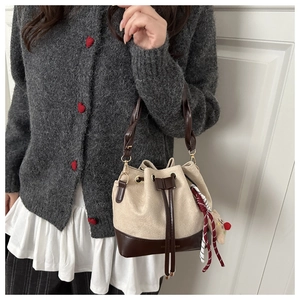Detail of a beige drawstring bucket bag with leather trim and a cute teddy bear charm