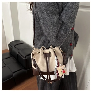 Detail of a beige canvas drawstring bucket bag with brown leather trim and bear charm