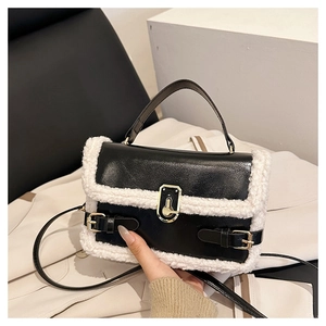 Close-up of black leather crossbody bag with white shearling trim and gold buckle detail
