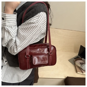 Detail of burgundy rectangular shoulder bag with white contrast stitching and laptop