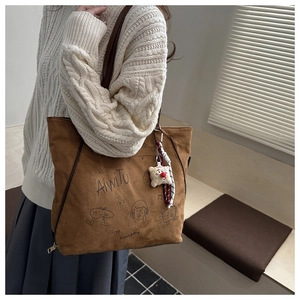 Detail der braunen Wildleder-Tote-Bag mit Graffiti und Plüschbären-Anhänger an der Schulter